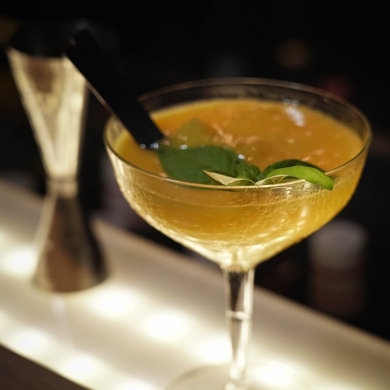 Goldgelber Mango Daiquiri in der Coupette, garniert mit frischem Basilikum