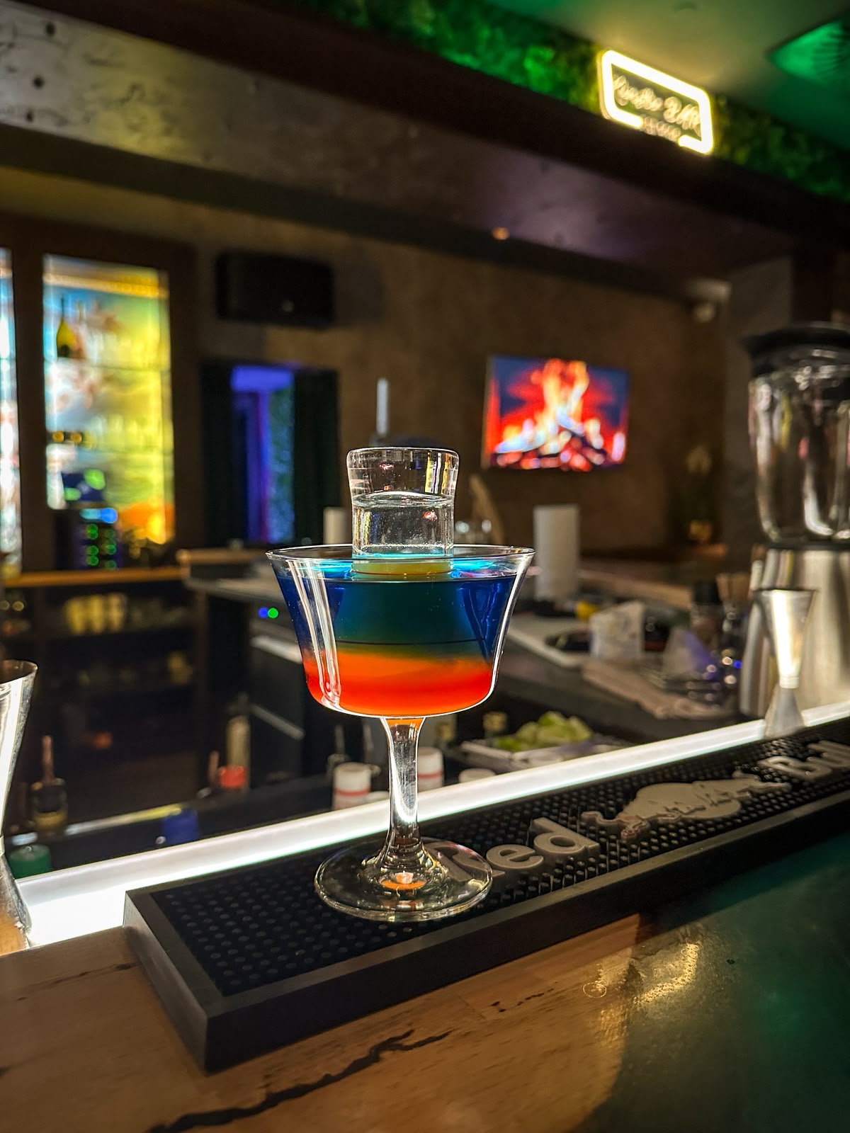 Geschichteter Cocktail in Blau und Orange in der Coupette mit aufgesetztem Shotglas