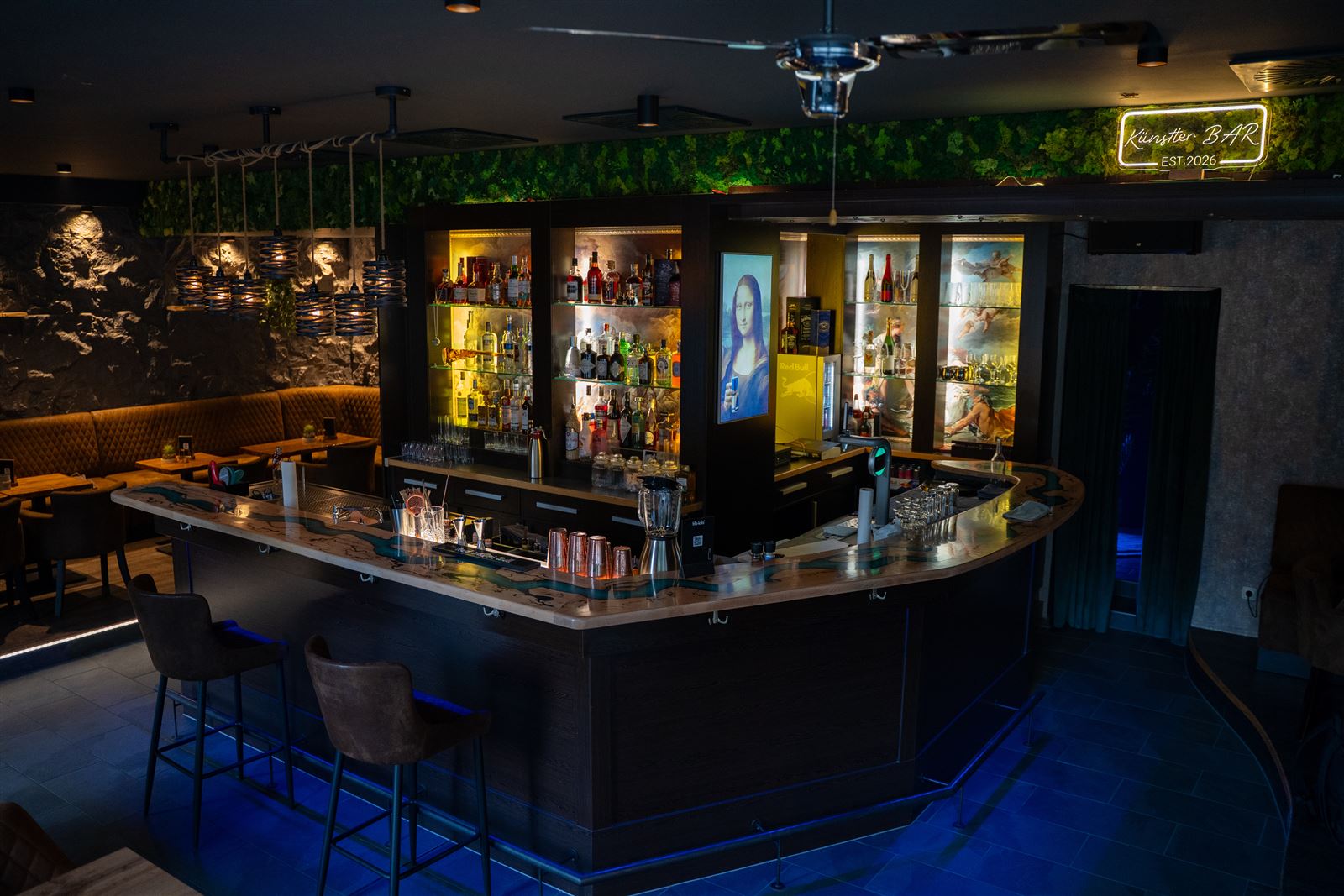 Der geschwungene Tresen der Künstlerbar mit beleuchtetem Flaschenregal, Sitzecke und Neonschild